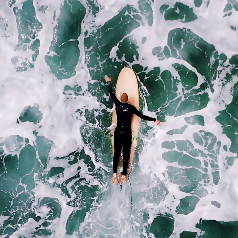 surfer paddling through turbulent water on a wooden surf board surrounded by white water.