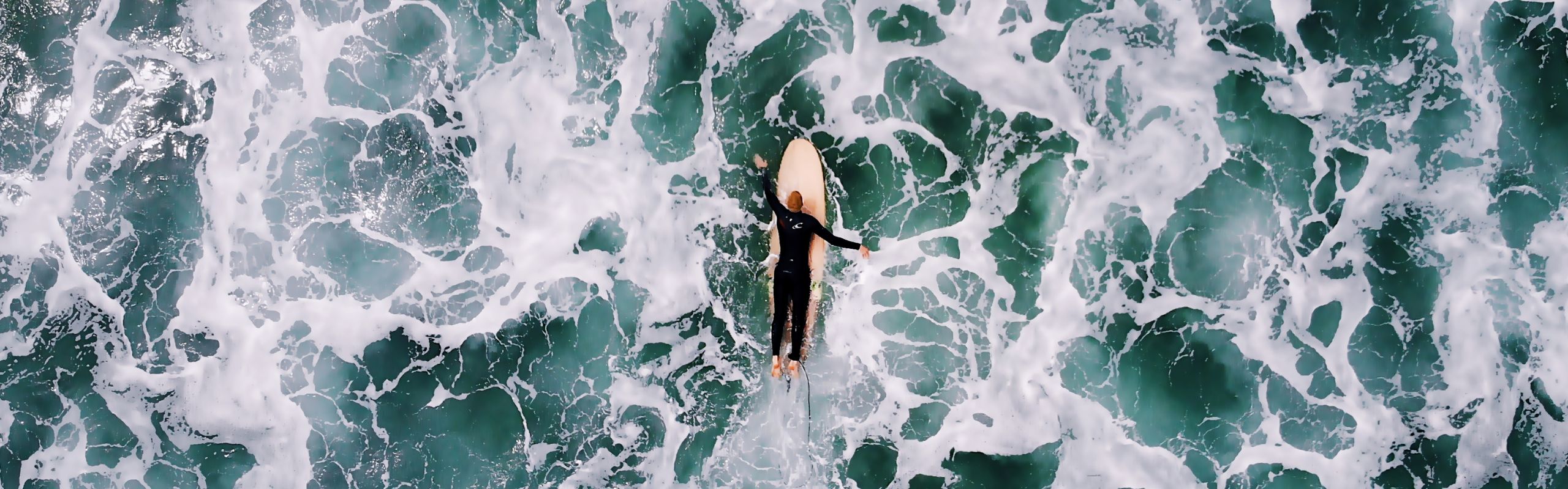 surfer paddling through turbulent water on a wooden surf board surrounded by white water.